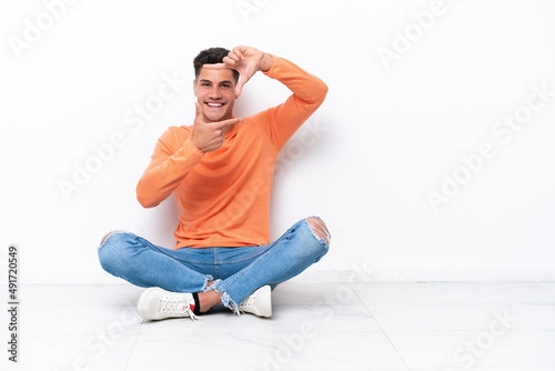 Young man sitting on the floor isolated on white background focusing face. Framing symbol