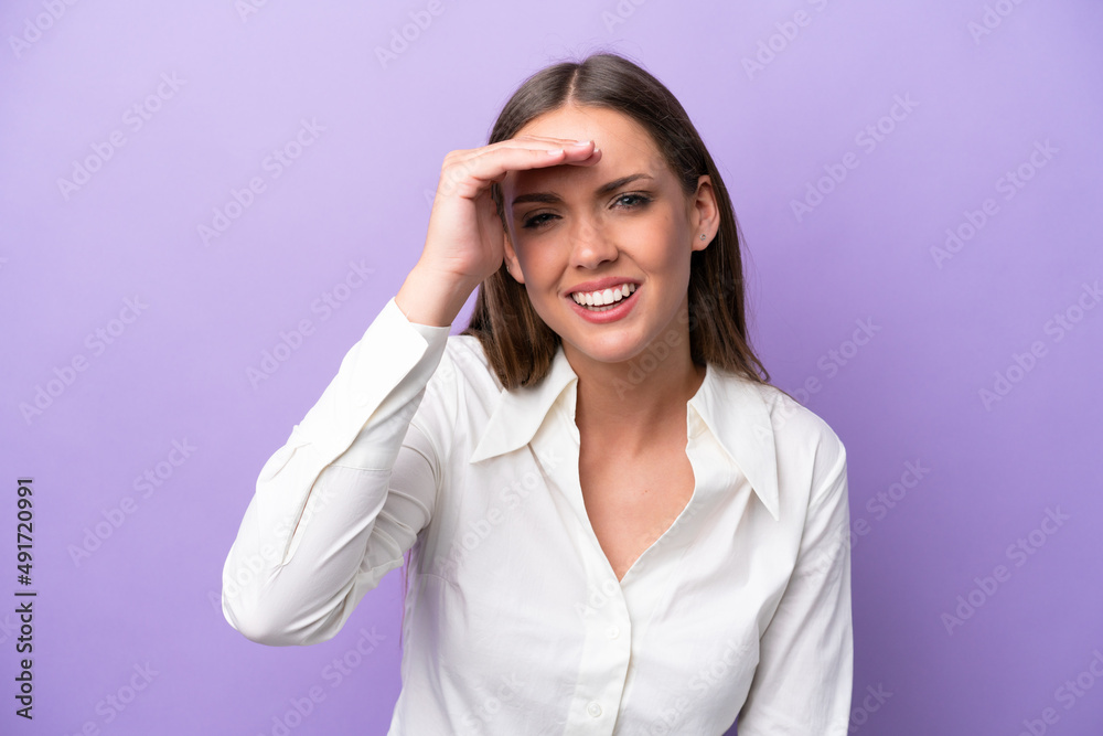 Young caucasian woman isolated on purple background looking far away with hand to look something Young caucasian woman isolated on purple background looking far away with hand to look something