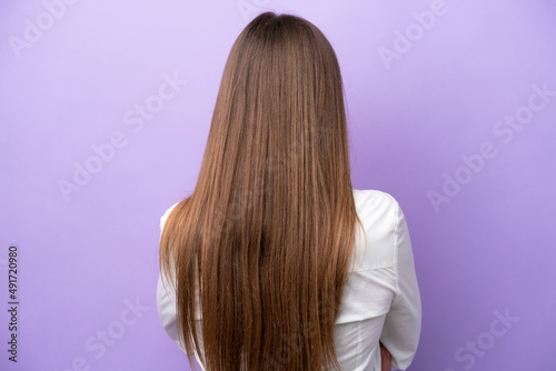 Young caucasian woman isolated on purple background in back position