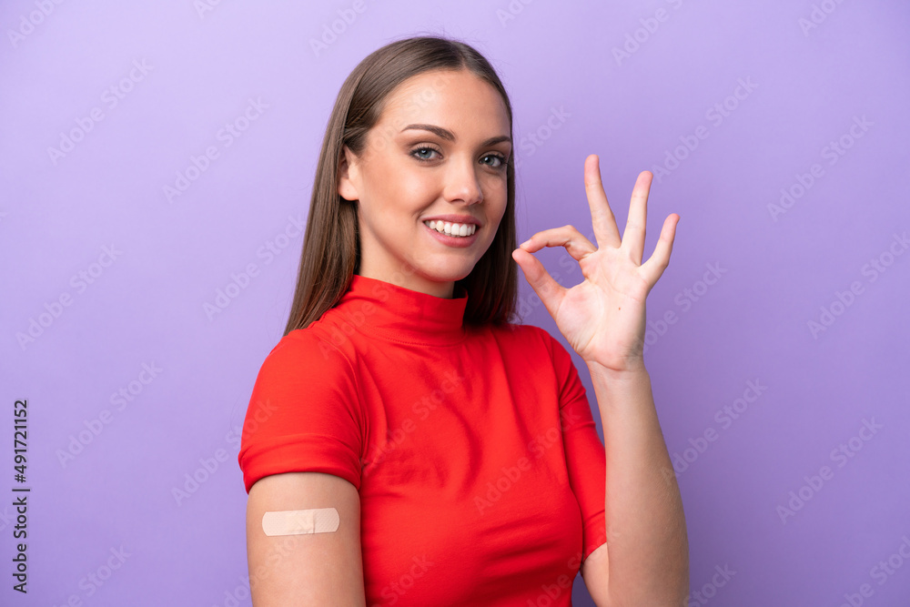 Young caucasian woman wearing band aid isolated on purple background showing ok sign with fingers Young caucasian woman wearing band aid isolated on purple background showing ok sign with fingers