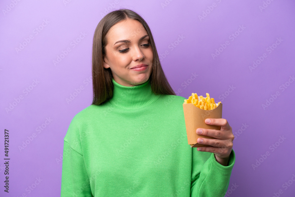 Young caucasian woman holding fried chips on purple background looking to the side and smiling Young caucasian woman holding fried chips on purple background looking to the side and smiling
