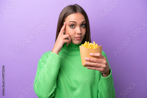 Young caucasian woman holding fried chips on purple background thinking an idea