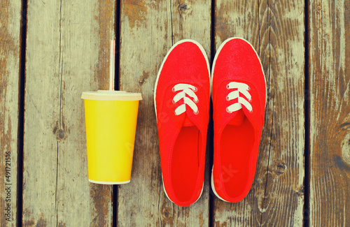 Summer image of red gumshoes with cup of juice on a wooden table or floor background, top view
