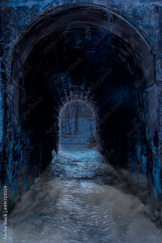 A low field of mist lays above the river of water flowing through the supposedly haunted Screaming Tunnel in the Niagara region of Ontario at night.