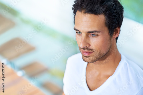 Hes clam and collected. A handsome young man sitting with his back agains a pane of glass.