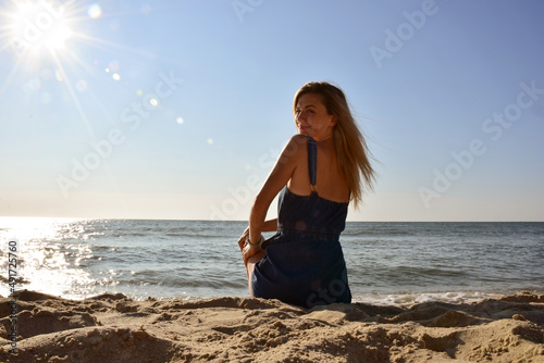 Young beautiful Caucasian woman sitting on the beach by the sea looking back
