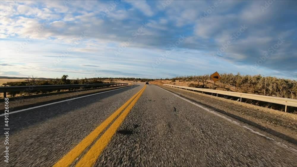 Rural road. Point of view of a car speeding the route in the countryside. The car drives towards sun setting in the horizon. The golden grassland and field at the sides of the route.