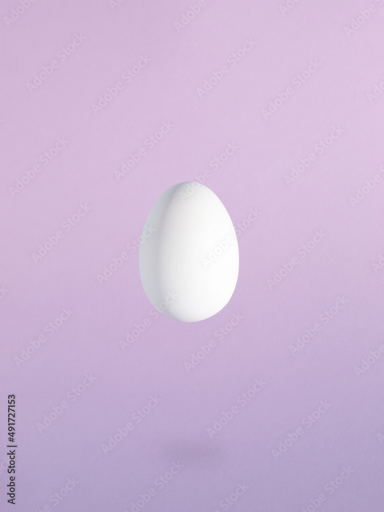 Minimal Easter composition with levitating white egg against pastel purple background. Minimal Easter composition with levitating white egg against pastel purple background.