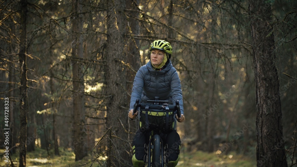 The woman travel on mixed terrain cycle touring with bike bikepacking outdoor. The traveler journey with bicycle bags. Stylish bikepacking, bike, sportswear in green black colors. Magic forest park.