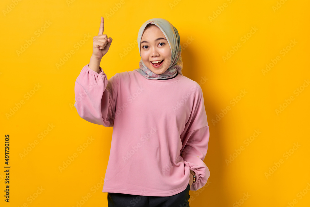 Shocked young Asian woman in pink shirt pointing fingers up having a good idea on yellow background Shocked young Asian woman in pink shirt pointing fingers up having a good idea on yellow background