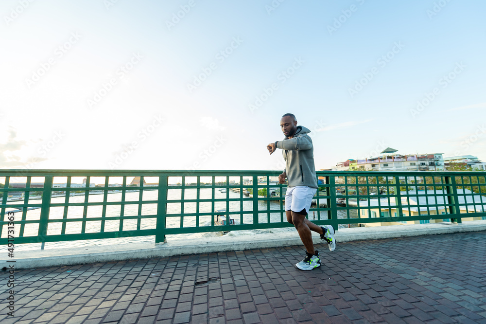  Confidence African man in sportswear and smart watch jogging exercise on the bridge in the city at summer sunset. Strong male athlete enjoy outdoor activity lifestyle sport training running workout. 