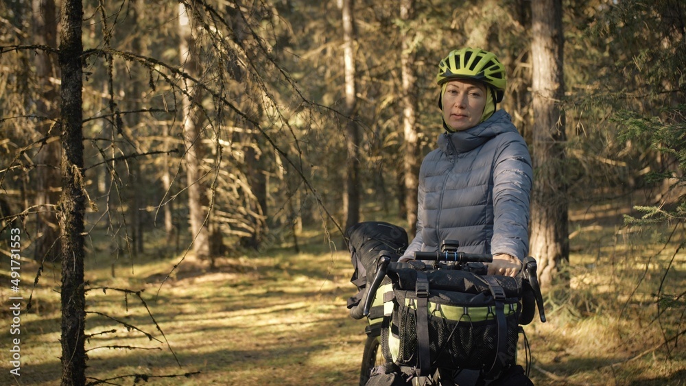 The woman travel on mixed terrain cycle touring with bike bikepacking outdoor. The traveler journey with bicycle bags. Stylish bikepacking, bike, sportswear in green black colors. Magic forest park. The woman travel on mixed terrain cycle touring with bike bikepacking outdoor. The traveler journey with bicycle bags. Stylish bikepacking, bike, sportswear in green black colors. Magic forest park.