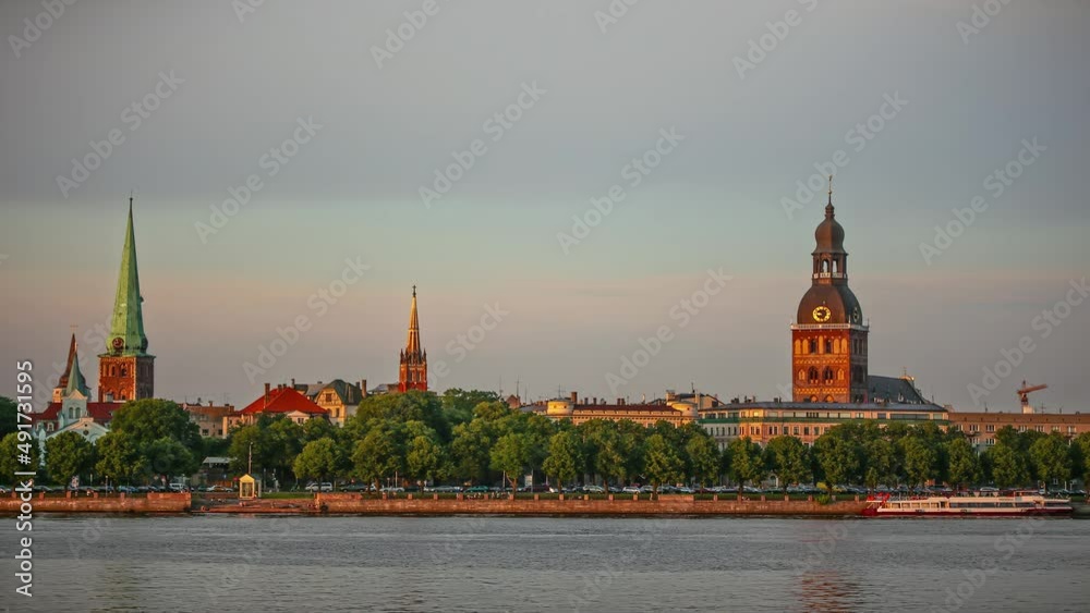 Time lapse shot of cruising boats on river and cars on coastal road in Riga during sunset light - Famous Cathedral and Tower in background Time lapse shot of cruising boats on river and cars on coastal road in Riga during sunset light - Famous Cathedral and Tower in background