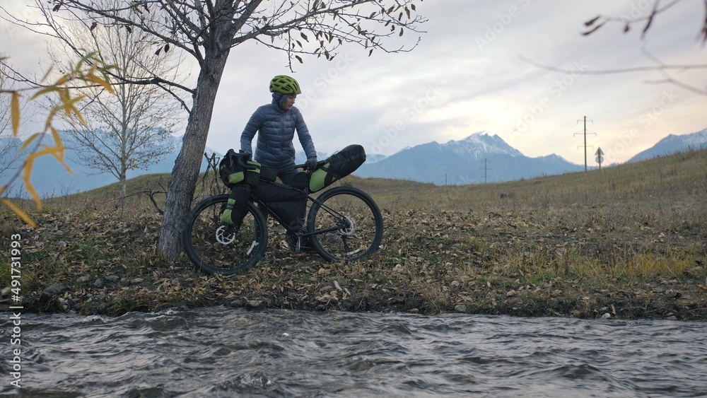 Obraz premium The woman travel on mixed terrain cycle touring with bikepacking. The traveler journey with bicycle bags. Sportswear in green black colors. The trip in magical autumn forest, river stream.