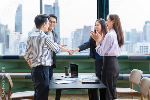 Asian business team leader congratulate his teammate employee for the outstanding achievement team performance by shaking hand in the modern office workplace with skyscraper view photo