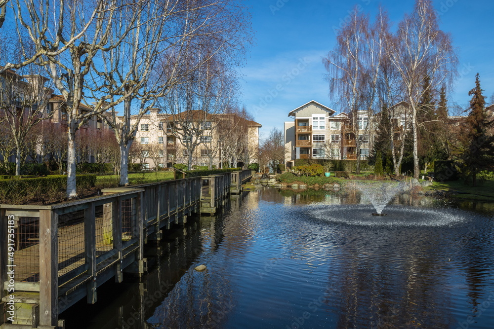 Residential District in Richmond City with pond and fountain, green grass bushes and trees in the territory of residential complex, Vanсouver, British Columbia 
