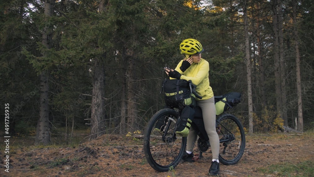 The woman travel on mixed terrain cycle touring with bike bikepacking outdoor. The traveler journey with bicycle bags. Sportswear in green black colors. Magic forest park. Make a selfie smartphone. The woman travel on mixed terrain cycle touring with bike bikepacking outdoor. The traveler journey with bicycle bags. Sportswear in green black colors. Magic forest park. Make a selfie smartphone.