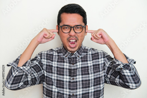 Portrait of adult Asian man screaming angry while closed his ears with finger photo