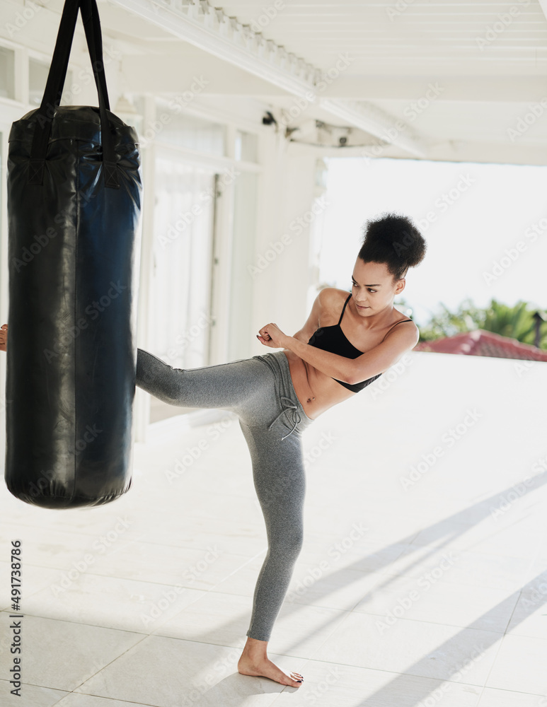 Keeping in tip top shape. Shot of a sporty young woman working out with a punching bag outside.