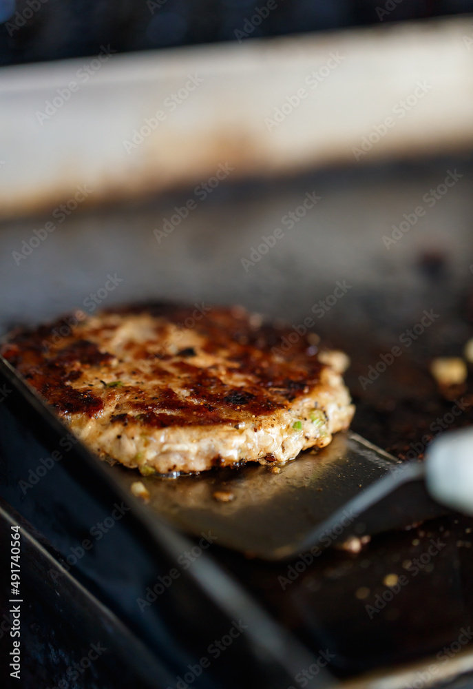 Closeup shot of delicious fresh baked burger bun with butter, minced cooked patty beef meat with margarine and pork bacon grilled on frying pan stove at dirty unsanitary local restaurant counter