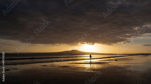 People walking at Milford beach at sunrise  Rangitoto Island in the distance  Auckland.