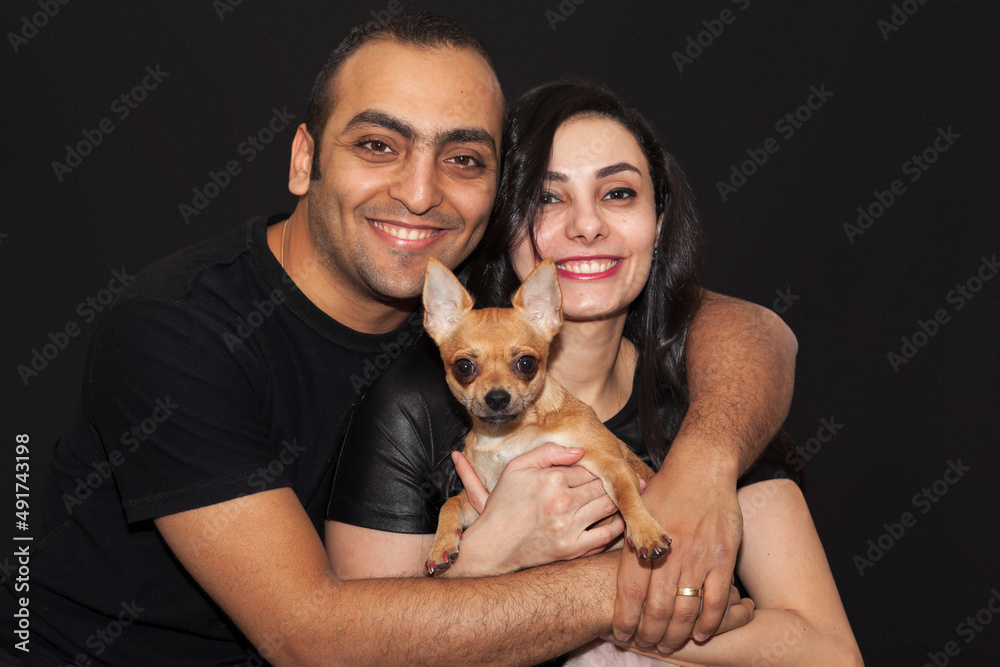 Studio portrait of a couple and their cute chihuahua breed dog. Black background. Studio portrait of a couple and their cute chihuahua breed dog. Black background.