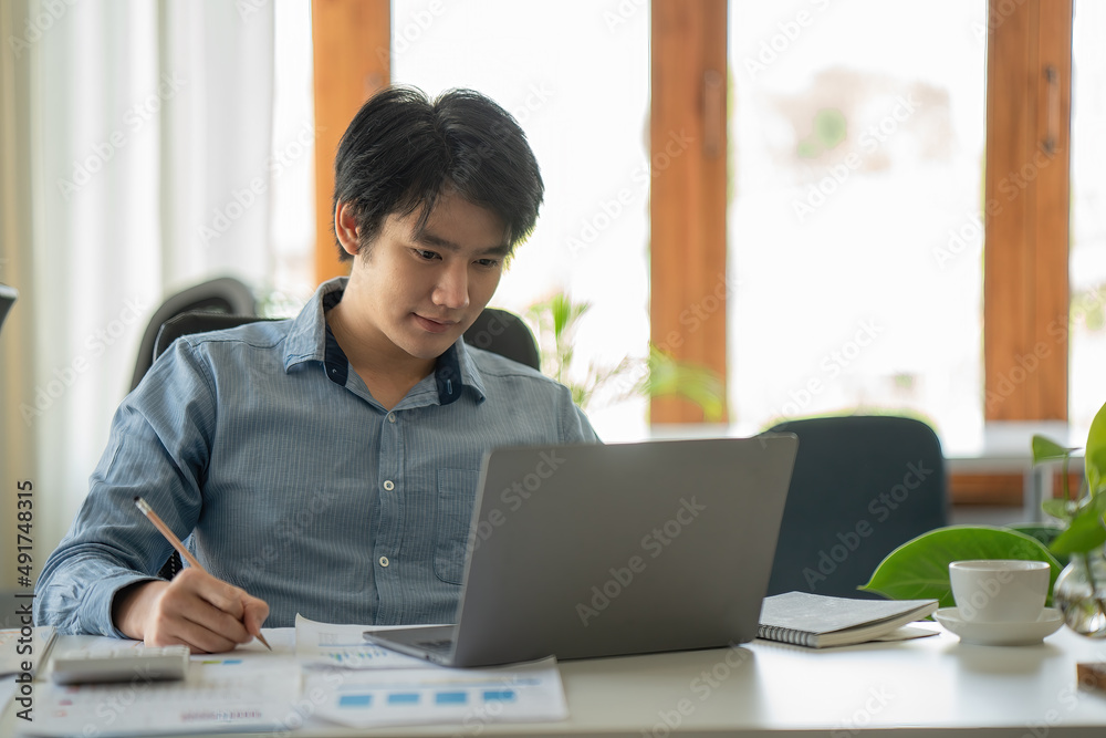 Asian businessman works in the office, calculates the report, the financier on paper works, uses the laptop and the calculator