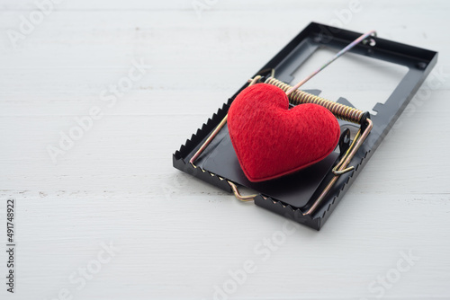 Red heart in a rat trap on white wooden background. Online internet romance scam, swindler or valentine day in darkside concept. Love is bait or victim.