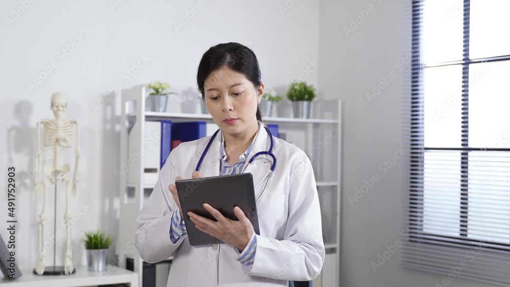 focused female doctor is looking away in contemplation while looking up information on the touchpad in her hands at a modern bright clinic. focused female doctor is looking away in contemplation while looking up information on the touchpad in her hands at a modern bright clinic.