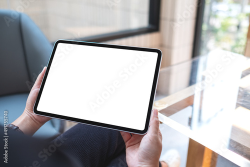 Mockup image of a woman holding digital tablet with blank white desktop screen in cafe