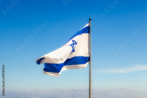 Flag of Israel at metal pillar waving on desert wind during hot sunny day.