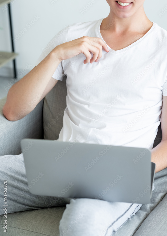 Virtual meeting. Casual man. Online conference. Happy unrecognizable guy sitting sofa with laptop holding on knees light room interior. Virtual meeting. Casual man. Online conference. Happy unrecognizable guy sitting sofa with laptop holding on knees light room interior.