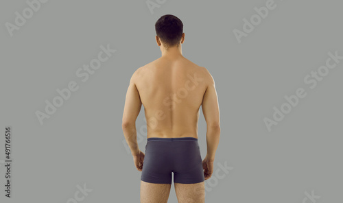 Rear view of fit sexy athletic man in underwear on grey studio background. Back shot of toned male model in underclothing wear show recommend briefs or boxers. Sport, fashion and style.