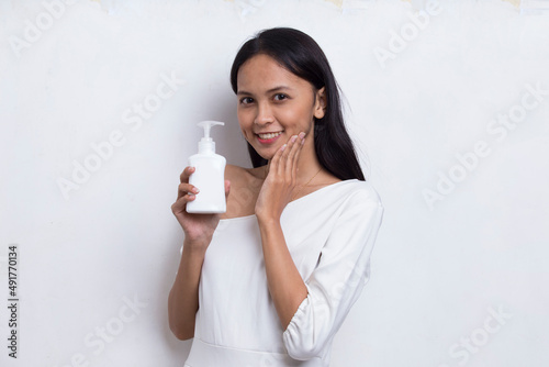 young beautiful asian woman putting skincare product to her face isolated on white background 