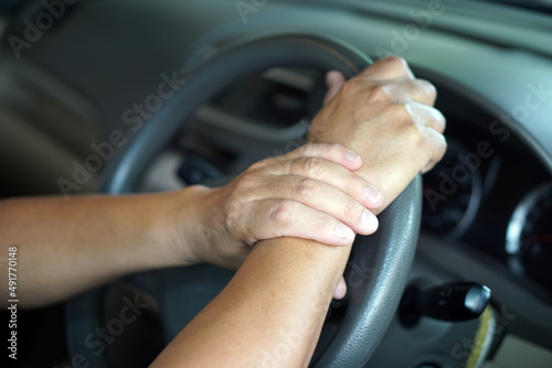 Left hand holds wrist right hand during holding a steering in car. Concept : Injury, pain or tired from driving. Unsafe driving during abnormal symptoms. Transport and healthcare. © Sanhanat