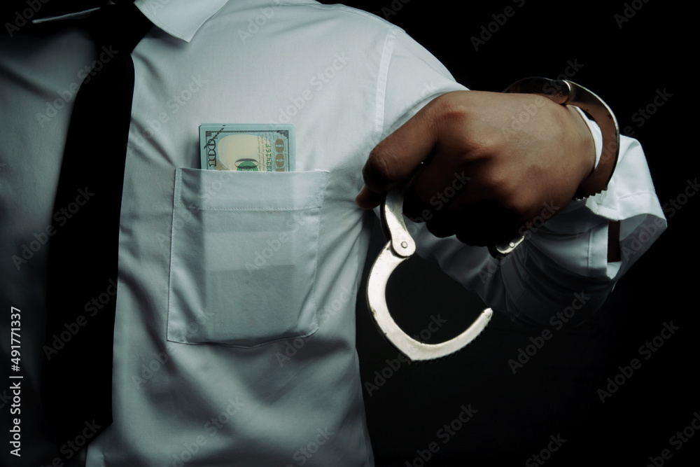Young businessman standing holding money and handcuffs attached to his arm Concept Corrupt police, bad cop, bribe police.