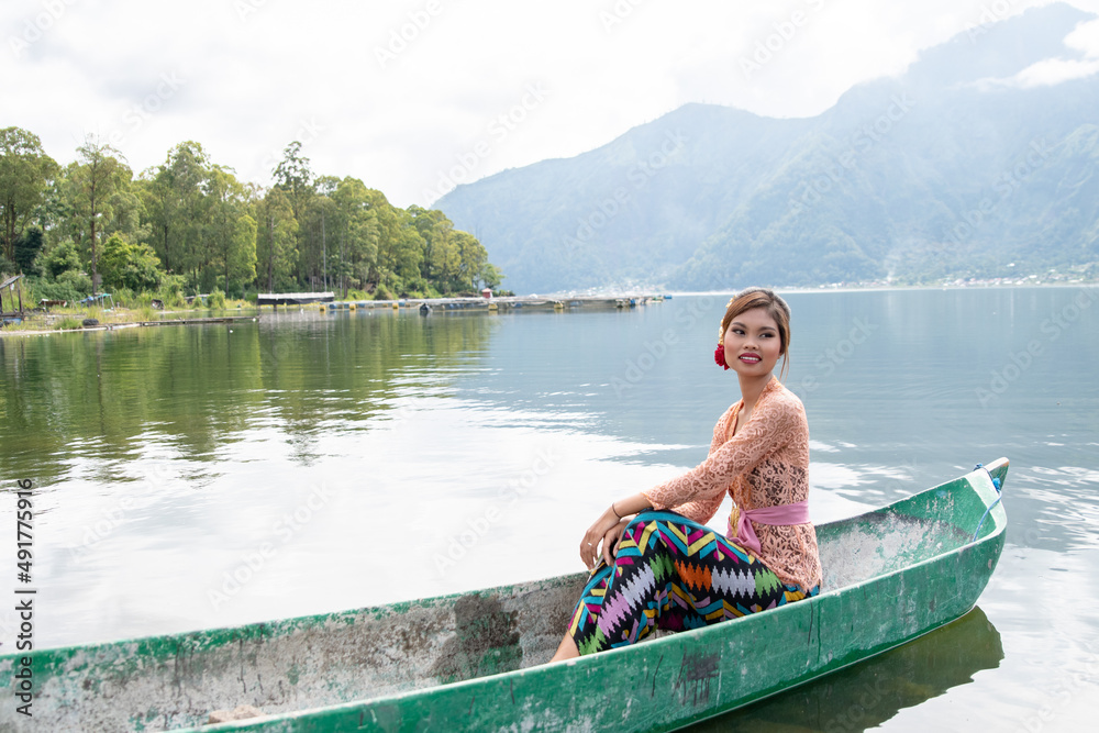 Young girl paddling on a wooden boat on a lake near a Bali temple.