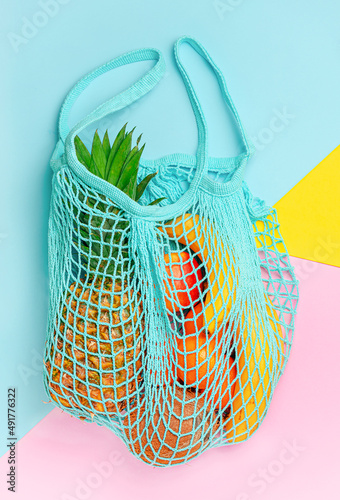 Different exotic fruits in reusable mesh bag on colorful background. Ecological lifestyle concept.