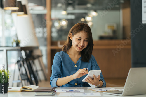 Portrait of asian business woman paying bills online with laptop in office. Beautiful girl with computer and chequebook, happy paying bills. Startup business financial calculate account concept photo