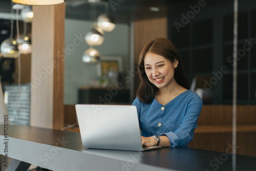 Young Asian female student sitting taking notes and using laptop computer at table.