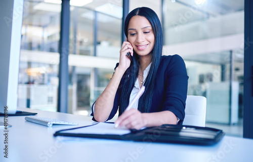 One signature gets it all. Shot of a young businesswoman going over paperwork and using a smartphone in a modern office.