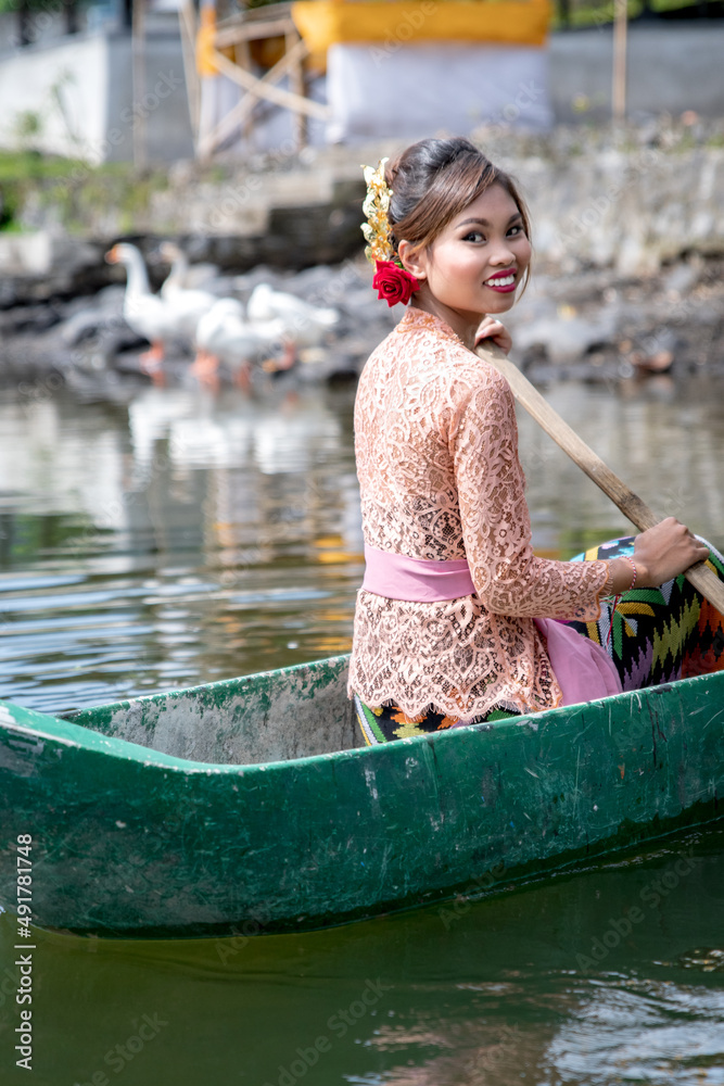 Young girl paddling on a wooden canoe in traditional clothes, and Hindu
