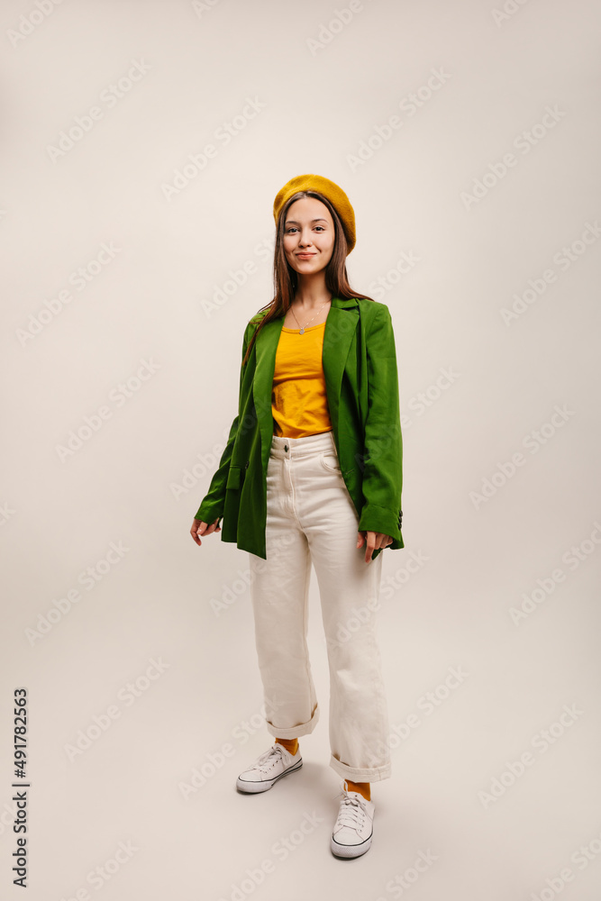 Full length young caucasian brunette girl in standing pose on white background. Pretty woman in stereotypical French clothes with beret. Elegant style, spring fashion trends.