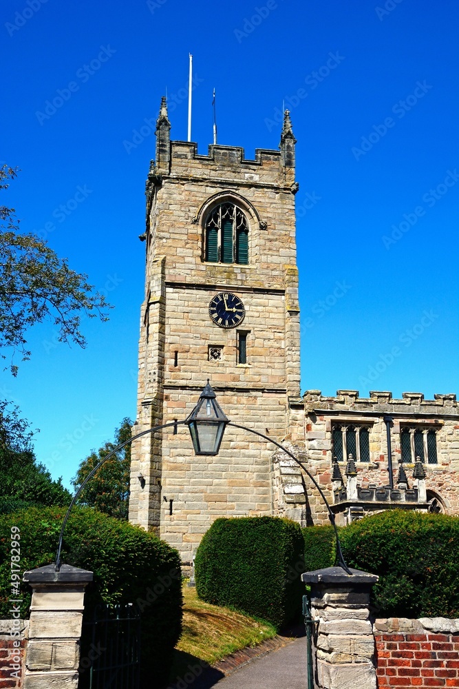 All Saints Church with an entrance arch in the foreground along Church Lane, Kings Bromley, Staffordshire, UK.