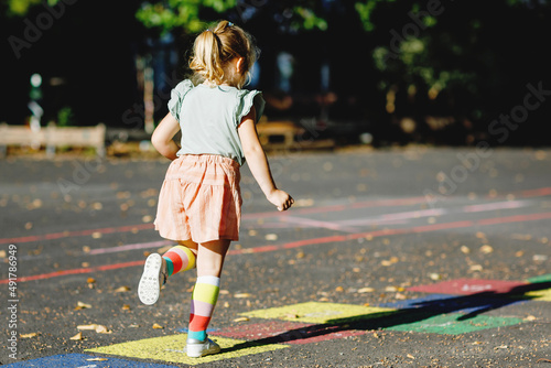 Cute little toddler girl playing hopscotch game drawn with colorful chalks on asphalt. Little active child jumping on playground outdoors on a sunny day. Summer activities for children. photo