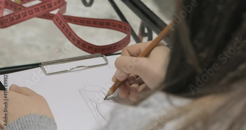the designer draws a sketch of an evening dress with a pencil on a transparent table near the measuring element. creating a design for a wedding dress at the factory. close-up