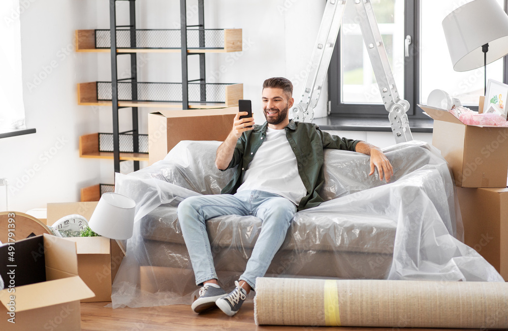 moving, people and real estate concept - happy smiling man with smartphone and boxes at new home