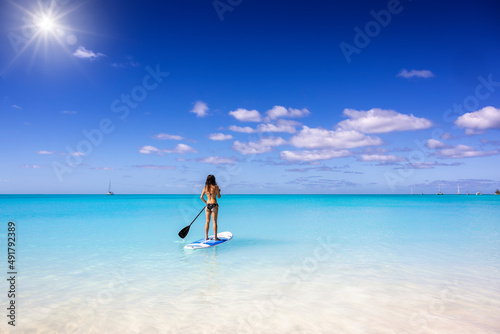 A woman exercising on a stand up paddle  SUP  board on turquoise  tropical sea