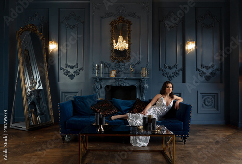 Beautiful brunette in a silver dress posing in a classic interior