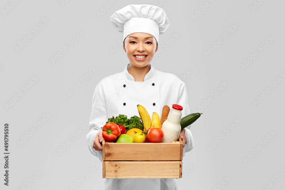 cooking, culinary and people concept - happy smiling female chef in toque holding food in wooden box over grey background cooking, culinary and people concept - happy smiling female chef in toque holding food in wooden box over grey background